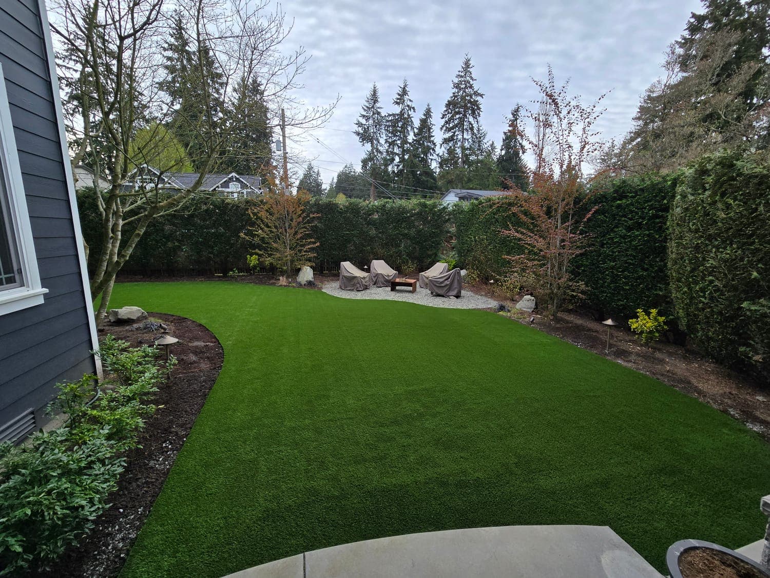 Lush artificial grass backyard lawn with patio seating installed by Synthetic Turf Solutions in the Greater Seattle Area