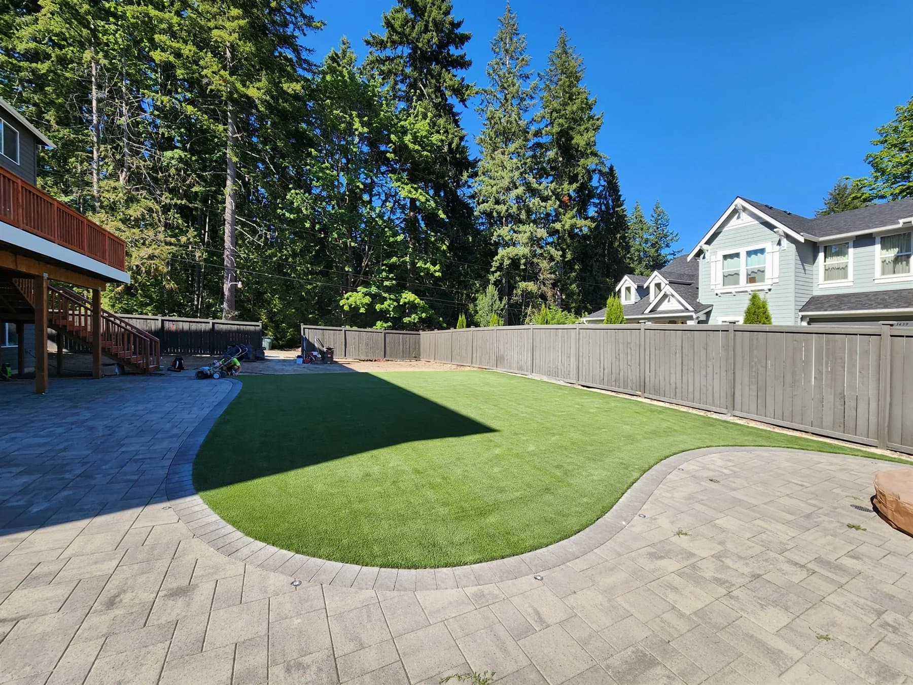 Curved backyard putting green installed beside a patio and fenced yard