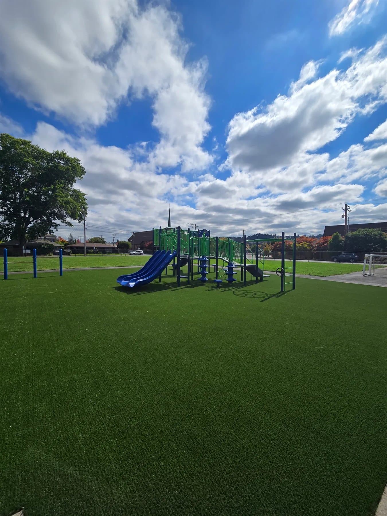 Open playground turf field with play equipment under a bright blue sky