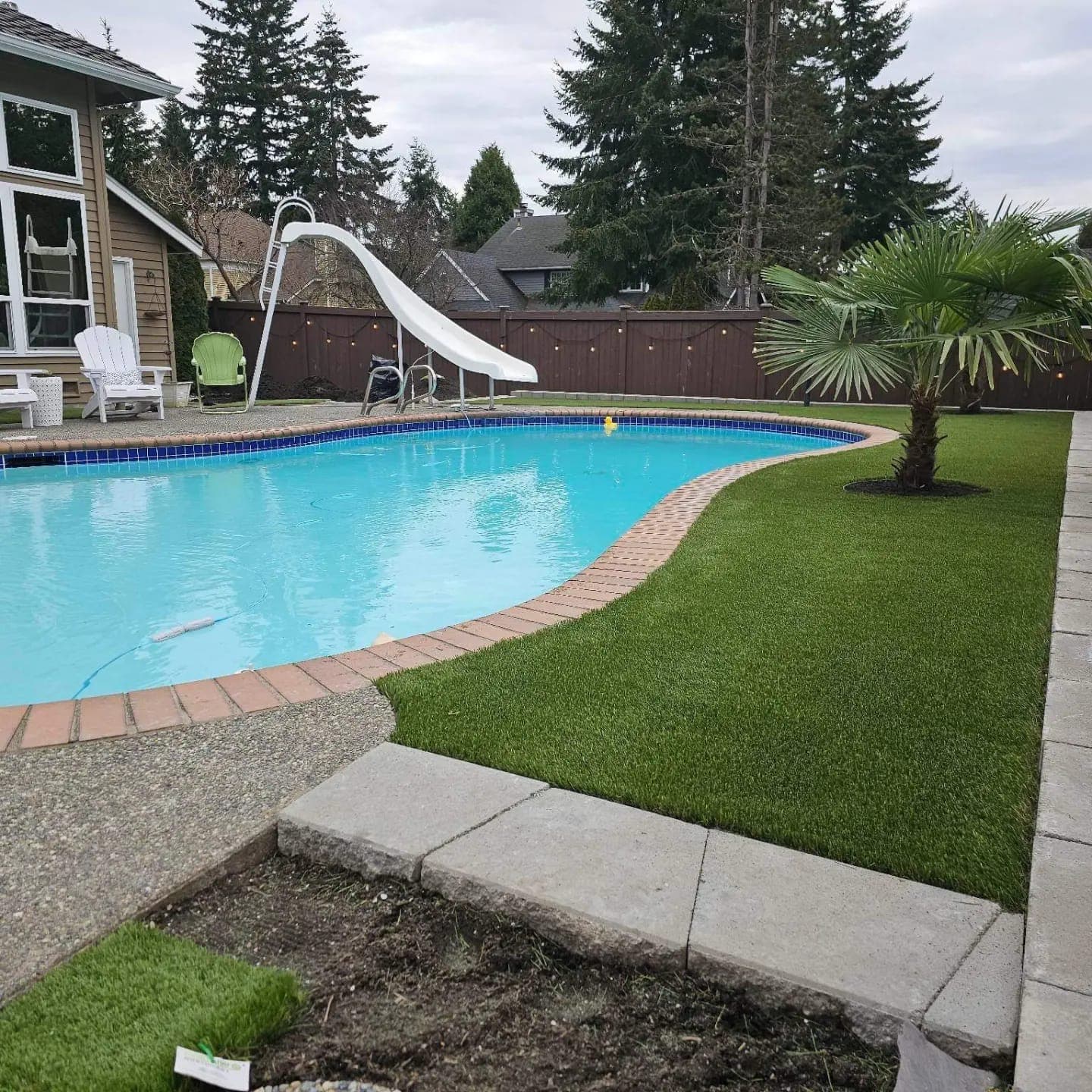 Artificial grass surrounding a backyard pool with a water slide and clean borders