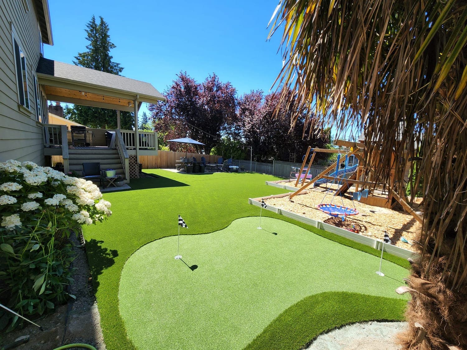 Backyard with a curved putting green, a play set, and an artificial lawn