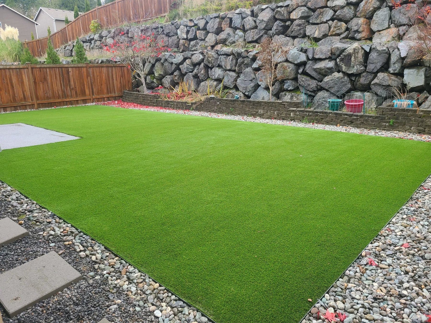 Fresh artificial lawn bordered by a retaining wall, gravel beds, and a wood fence