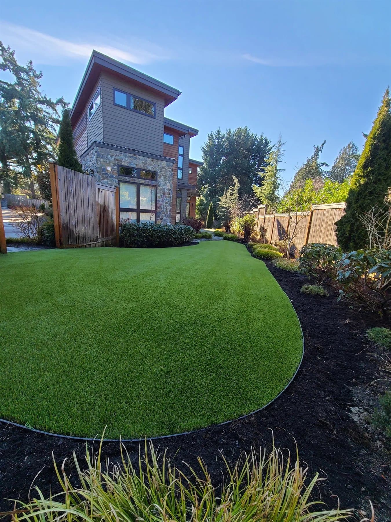 Shaded backyard putting green tucked beside landscaping and a tall privacy fence