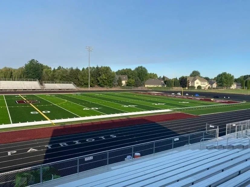 Synthetic turf sports field installed in a stadium with track lanes and bleachers